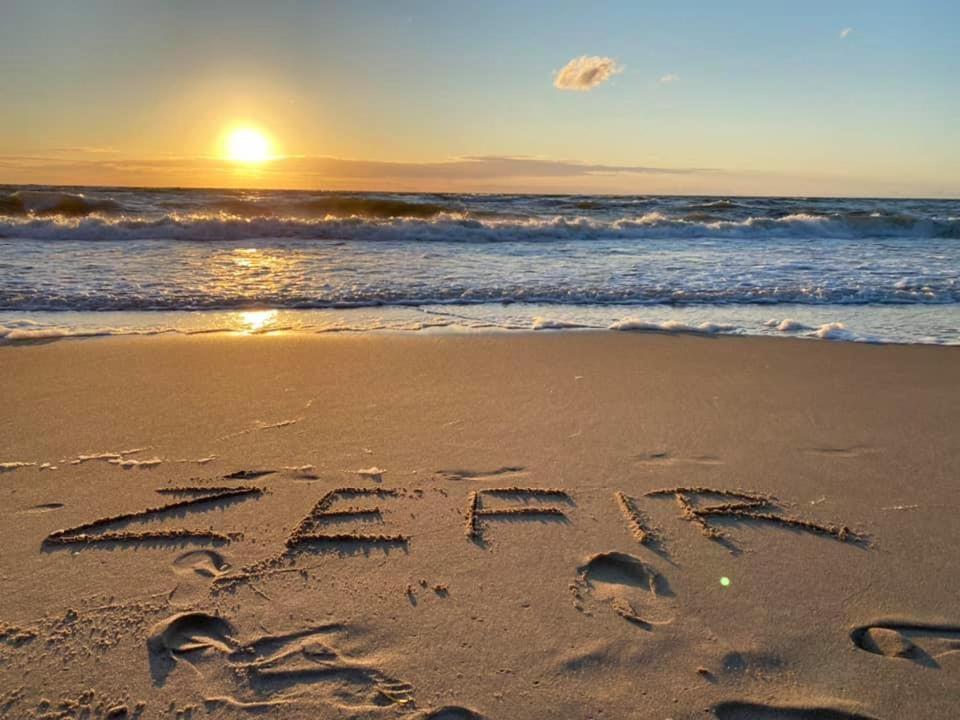 Zachód słońca na plaży w Dąbkach — napis "ZEFIR" wypisany w piasku.