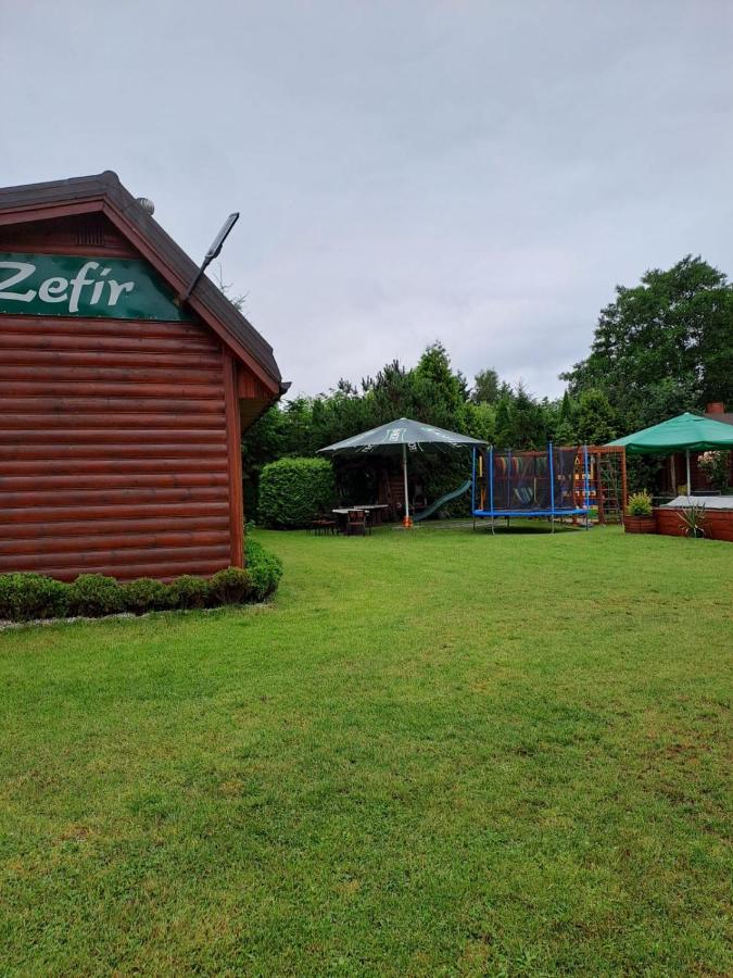 Drewniany domek z szyldem "Zefir" i widokiem na plac zabaw.